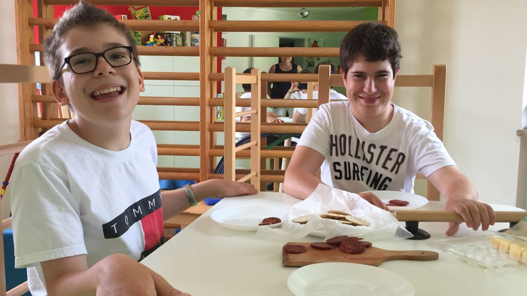 Zwei lächelnde Teenager sitzen an einem weißen Tisch in einem hellen Raum , vor einer Holzsprossenwand.